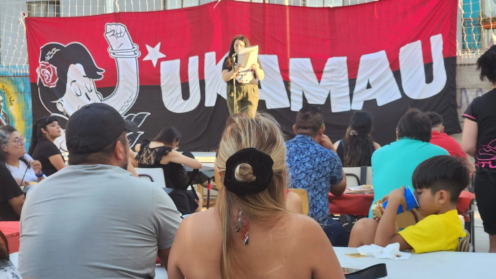 Familias reunidas en una actividad del Barrio Maestranza, frente a un lienzo del Movimiento de Pobladores Ukamau.
